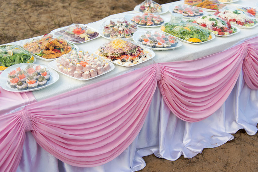 Buffet catering for a wedding party on the beach on a white table with a pink drapery