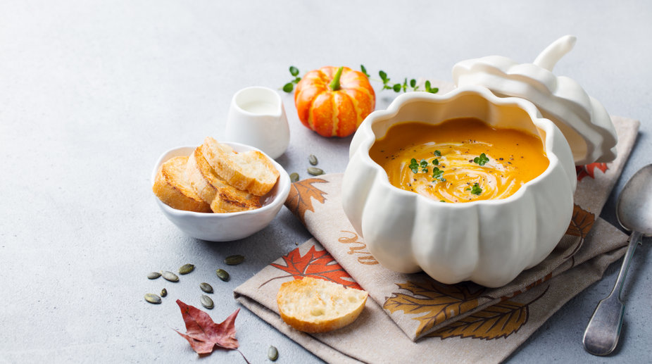 Pumpkin and carrot cream soup in bowl on grey stone