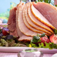 Honey ham on Easter table with eggs, flowers and decoration